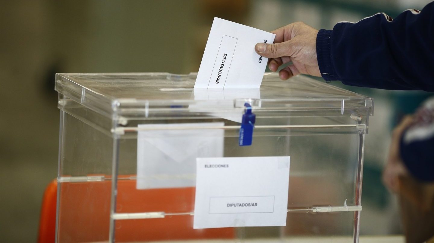 Una mano metiendo un sobre de votación en una caja