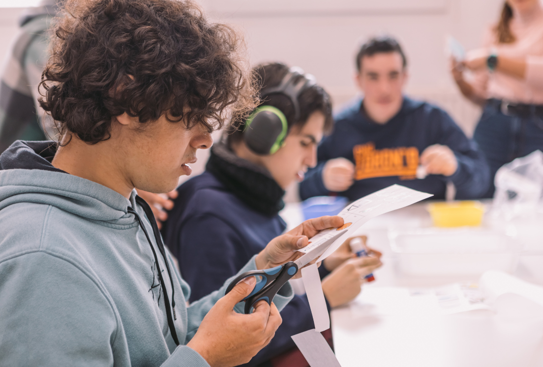 Un chico autista recortando un papel en una clase con más alumnos y alumnas