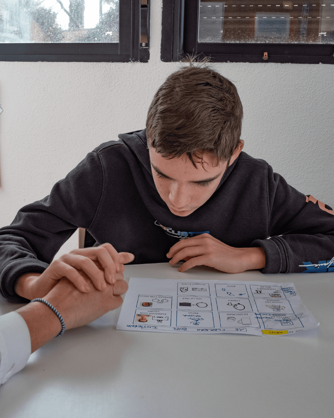 Niño en pupitre trabajando con pictogramas con su profesional
