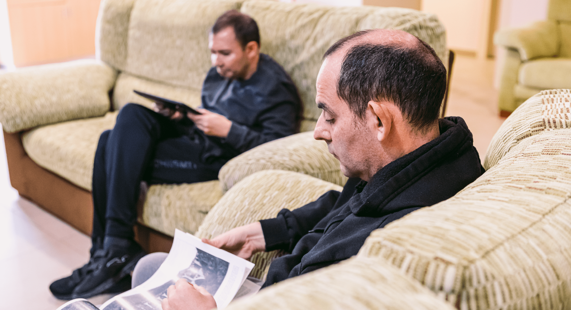 Dos adultos sentados en el sofa mirando una revista y su tablet.