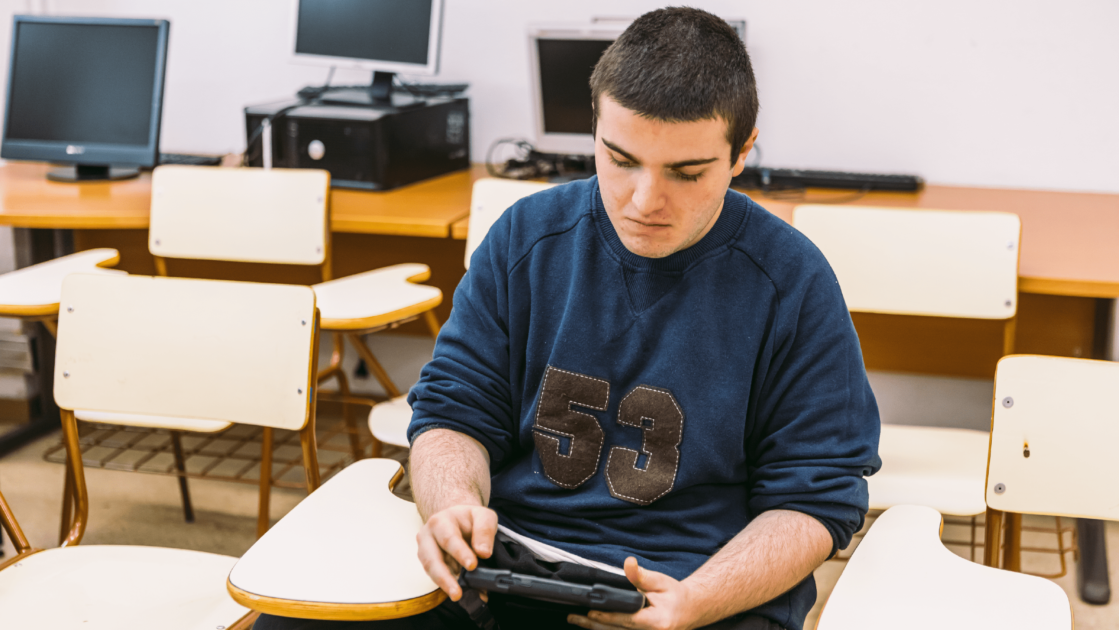 Chico sentado en una silla escolar con un tablet en la mano