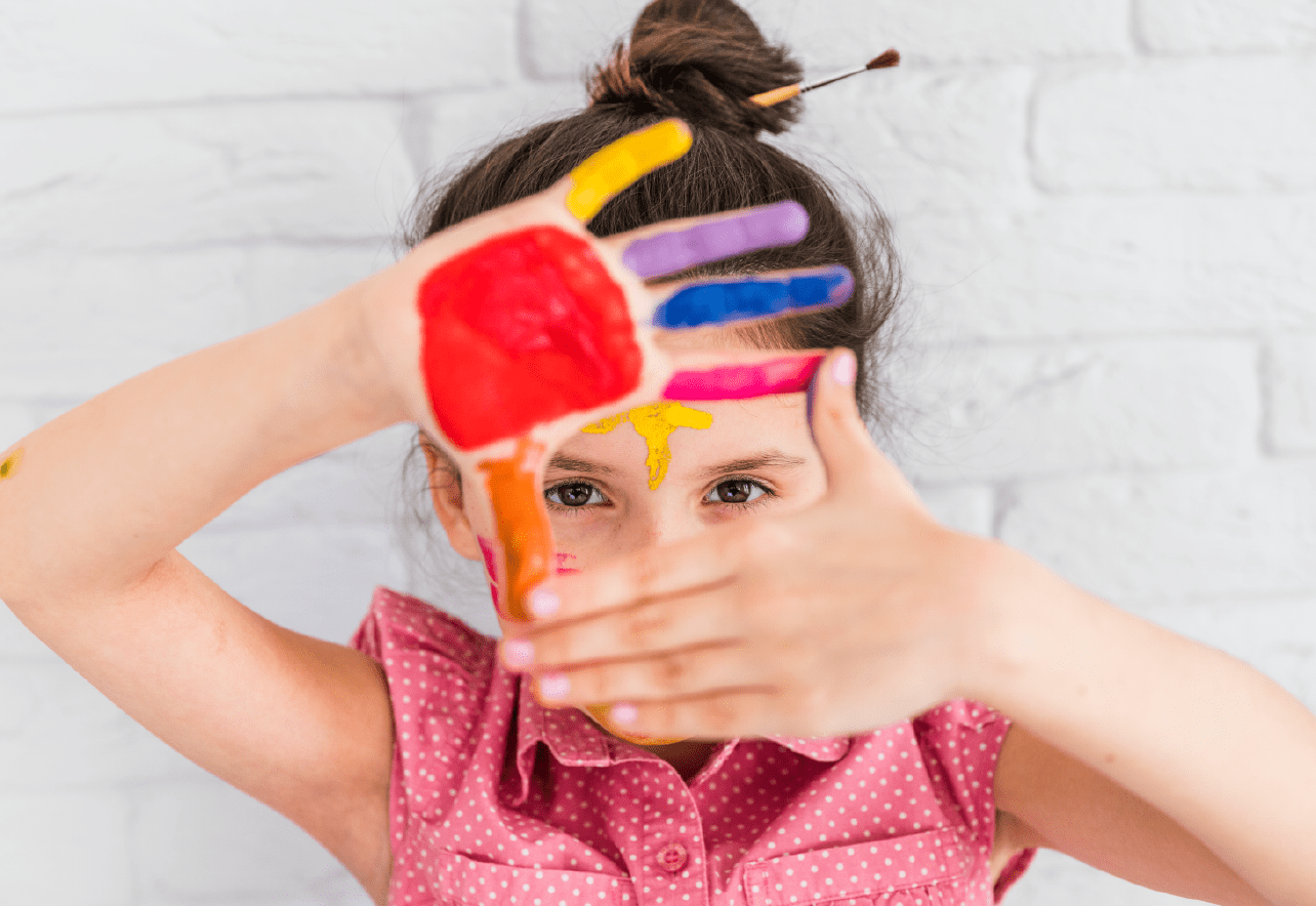 Una niña mirando a cámara con una de sus manos pintada de colores delante de su cara
