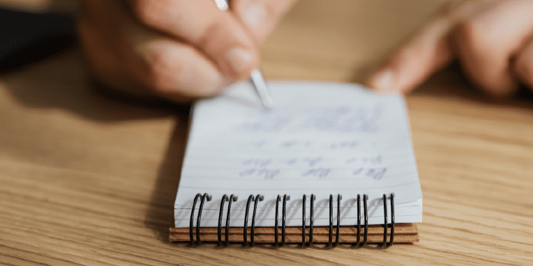 Miniatura de una mano escribiendo en una libreta