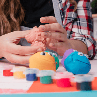 Dos manos amasando plastilina con varias bolas de plastilina de colores en la mesa.
