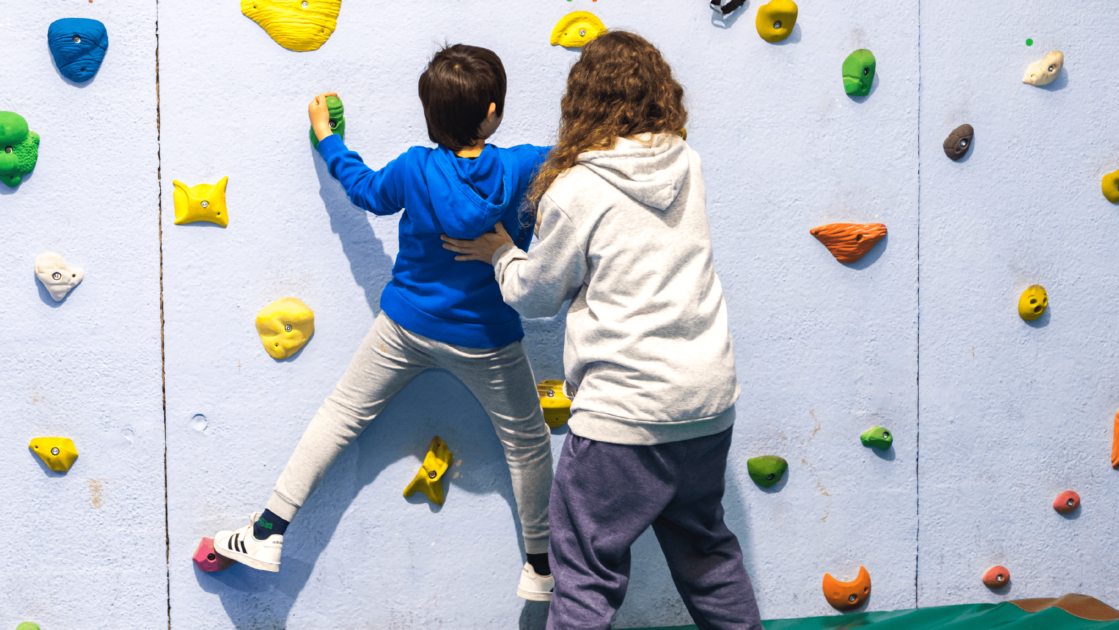 Profesional ayudando a un niño practicando escalada deportiva en un gimnasio.