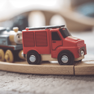 Imagen de un camión rojo de juguete seguido de un tren con cara sonriente.