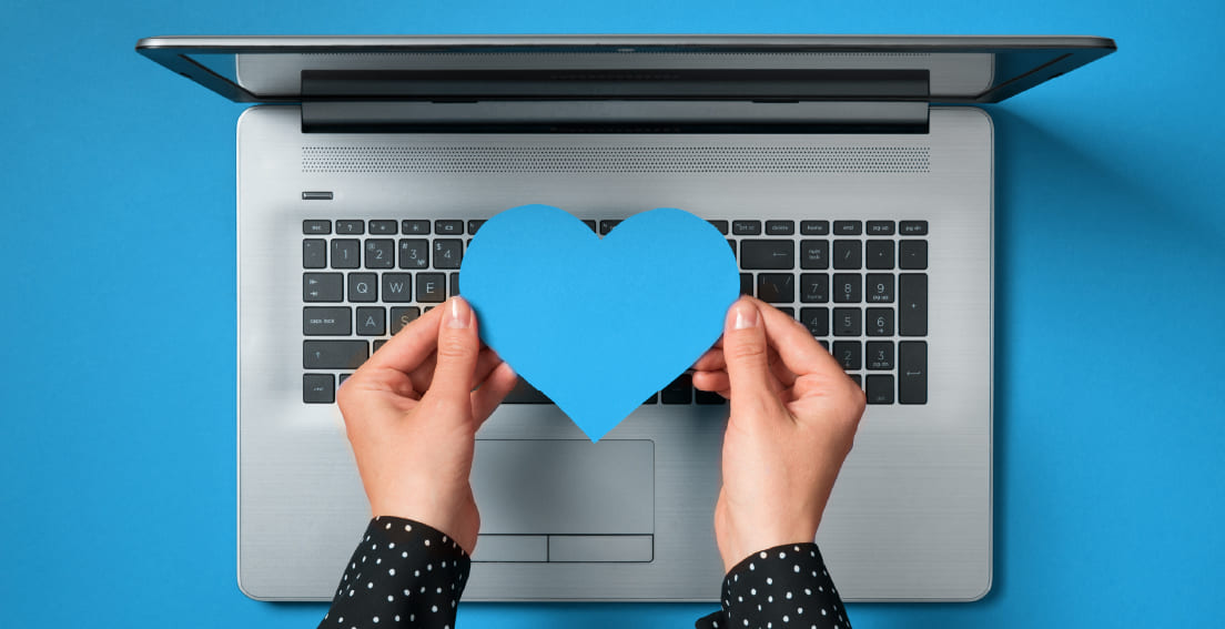 Unas manos sujetando un corazón de papel azul frente a un ordenador portátil