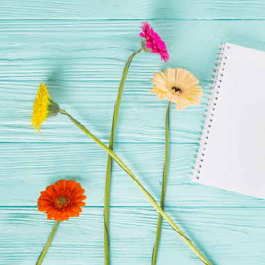Miniatura de unas flores de colores junto a un cuaderno en un fondo azul.