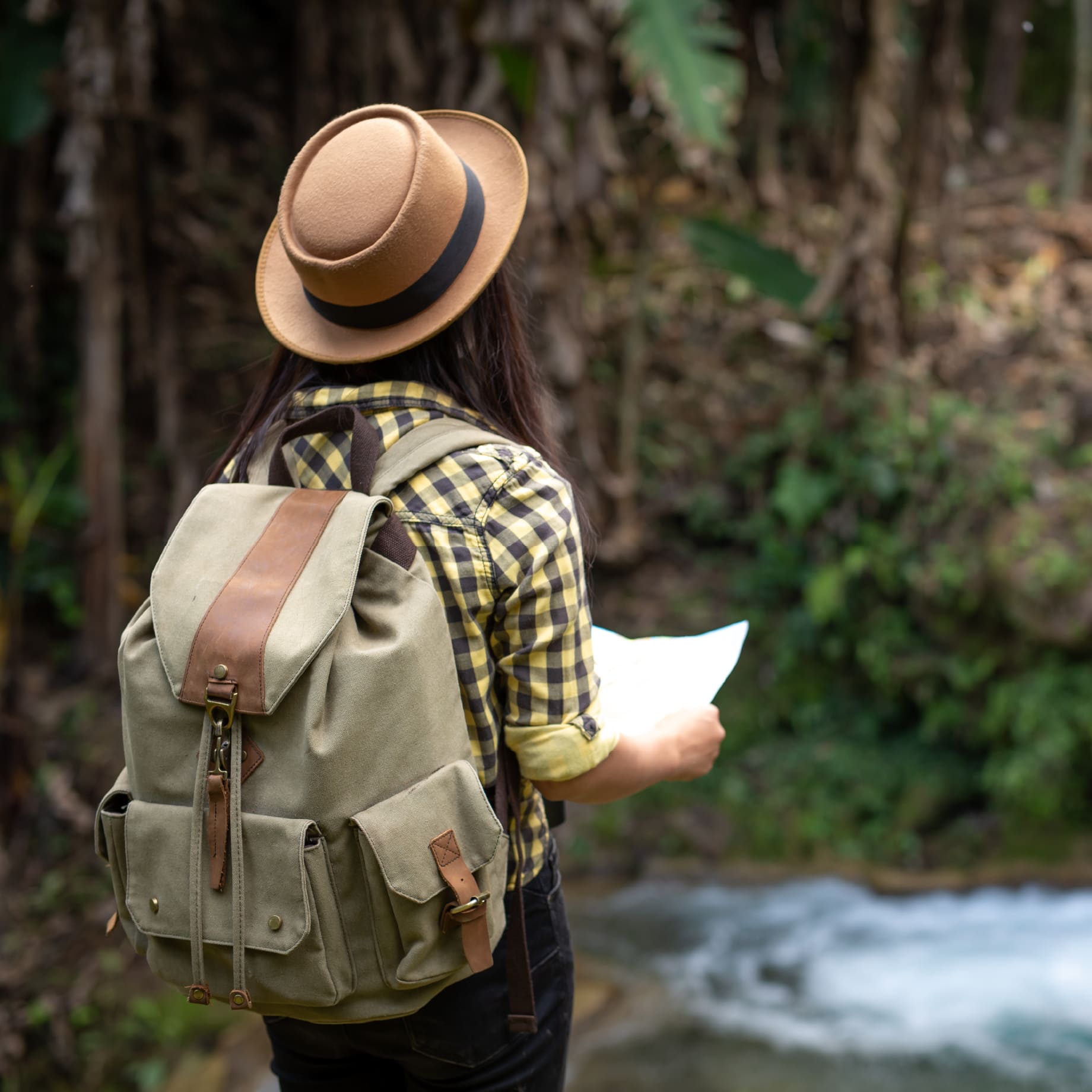 Persona frente a un paisaje natural con una mochila a la espalda, un sombrero y un mapa en la mano.