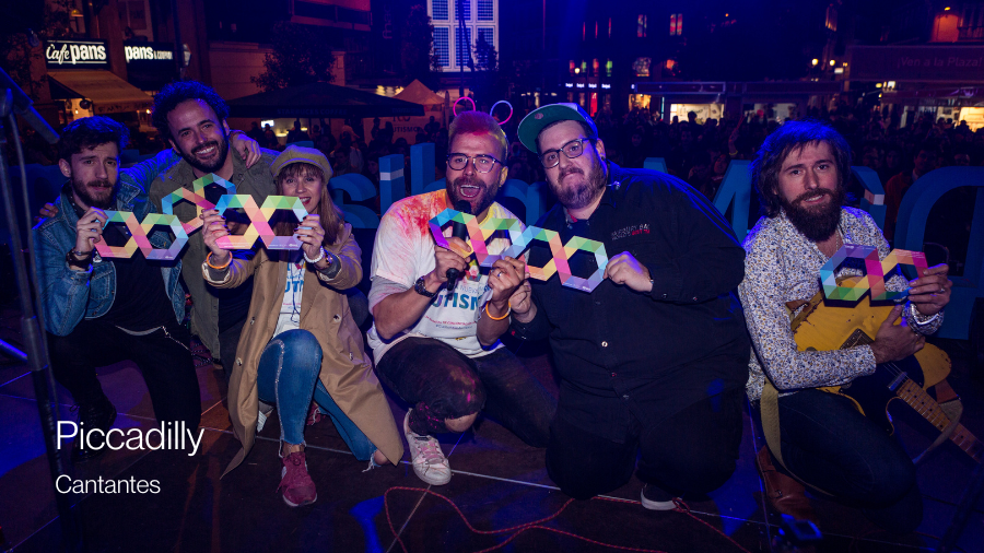 El grupo de música Piccadilly posando sobre un escenario cogiendo con un infinito multicolor
