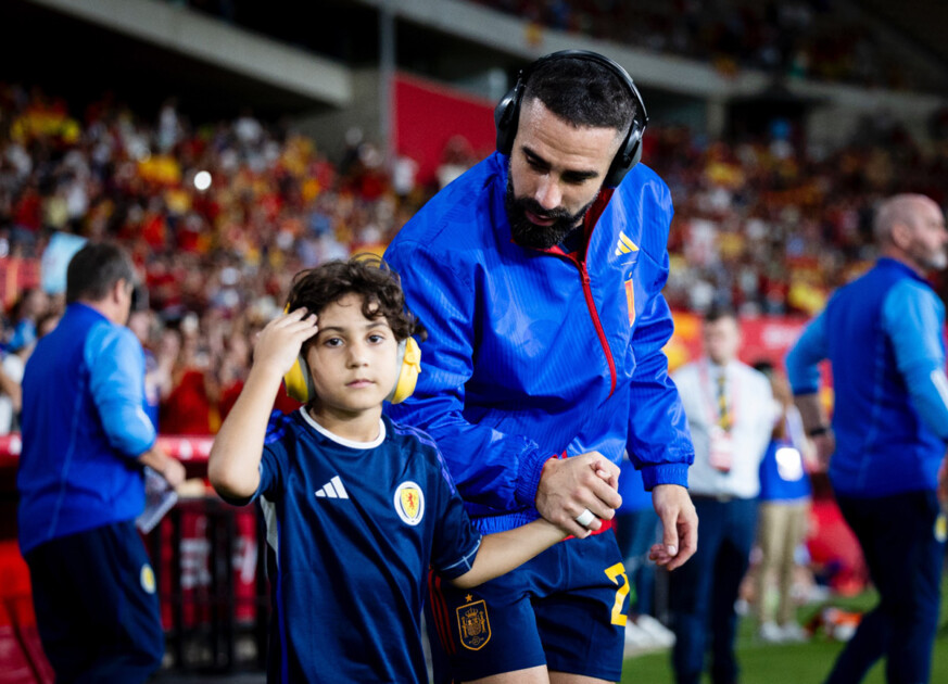 Un jugador de la selección masculina de fútbol de la mano con un niño autista que lleva cascos de reducción de ruido