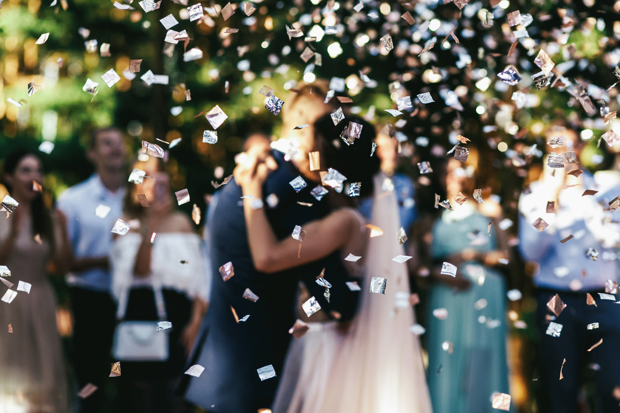 Confeti plateado con novios e invitados en una boda de fondo