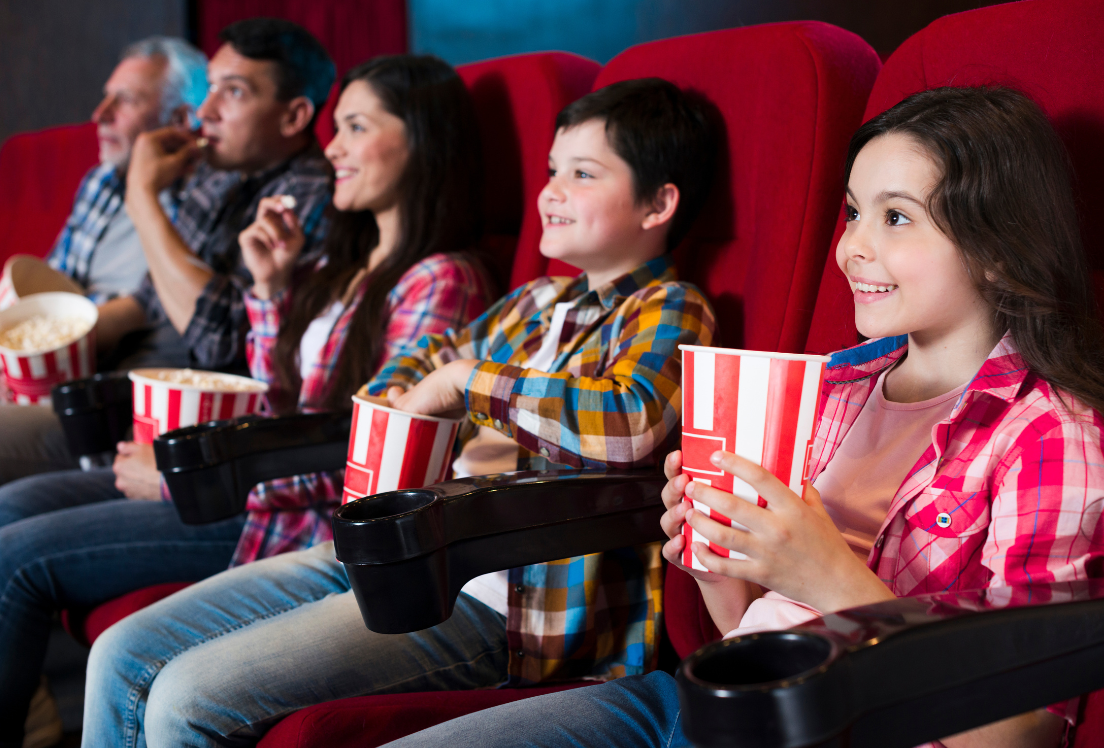 Tres personas adultas, un niño y una niña, comen palomitas en una sala de cine