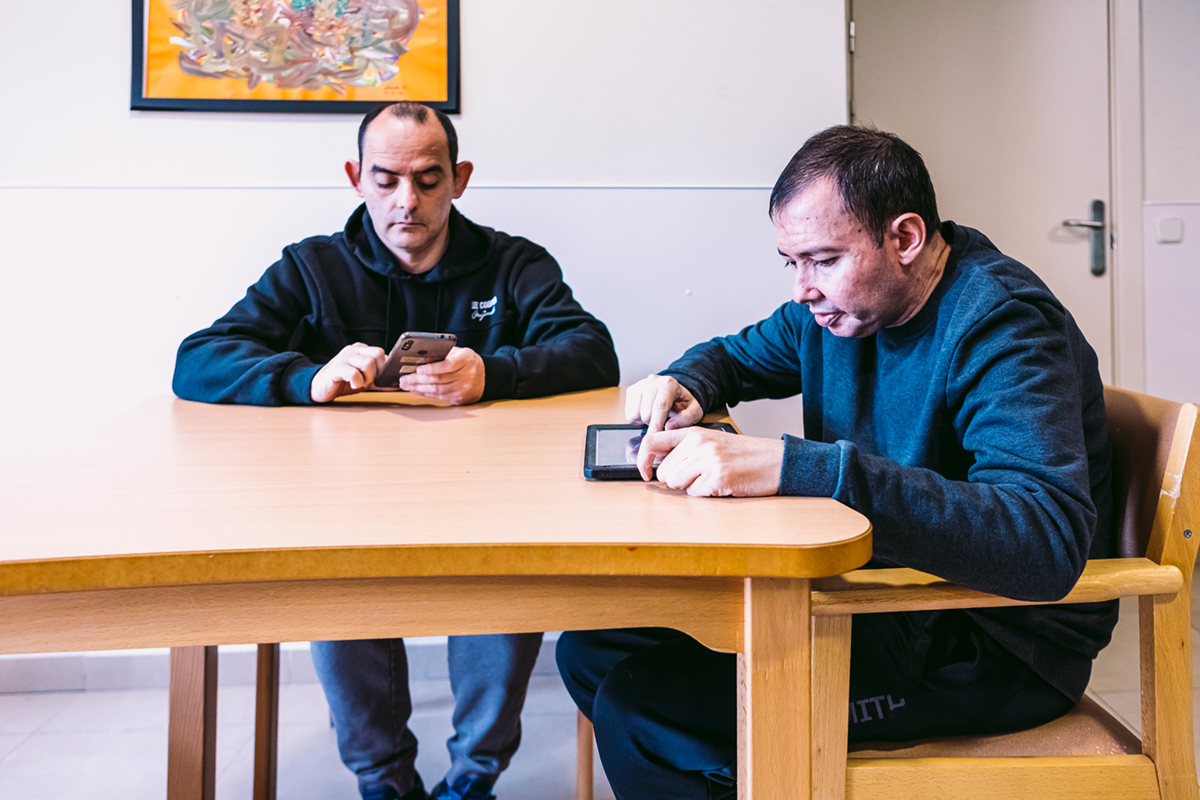 Dos hombres autistas sentados en una mesa utilizando dispositivos electrónicos