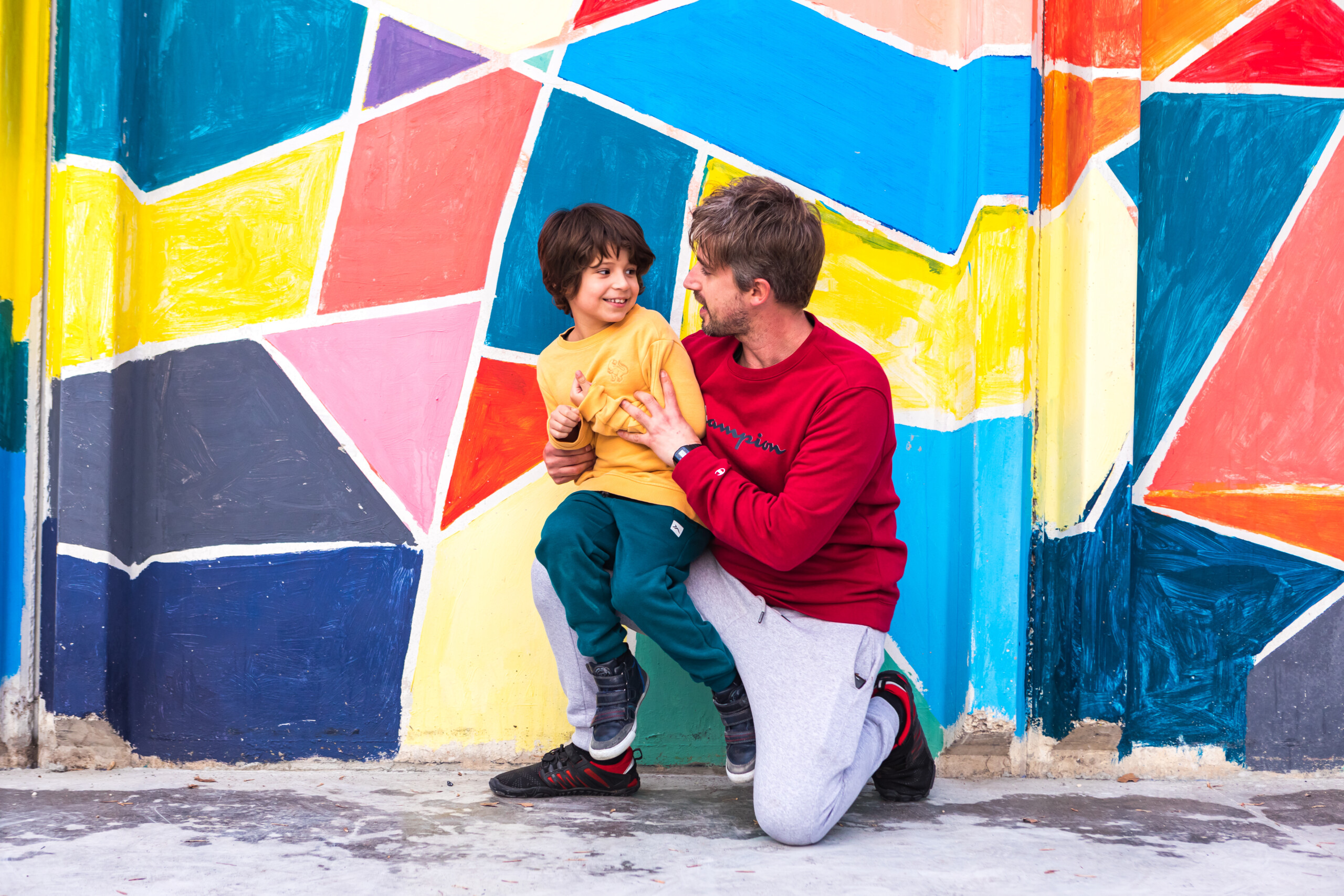 Un niño y un chico joven se miran sonriendo frente a una pared de colores