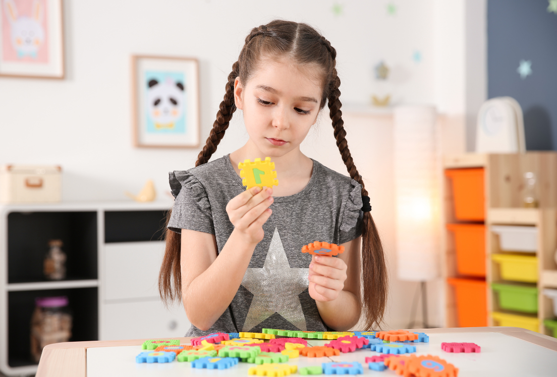 Una niña con trenzas juega con una fichas de colores en una mesa.