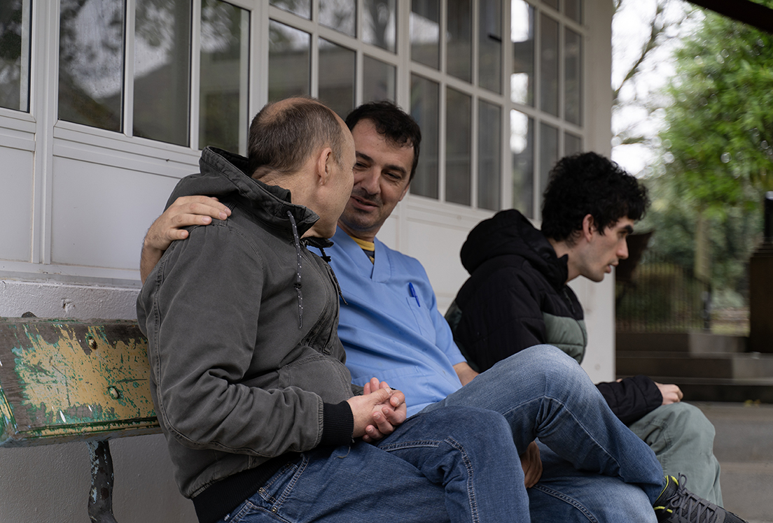 Dos hombres autistas junto a su cuidador sentados en un banco