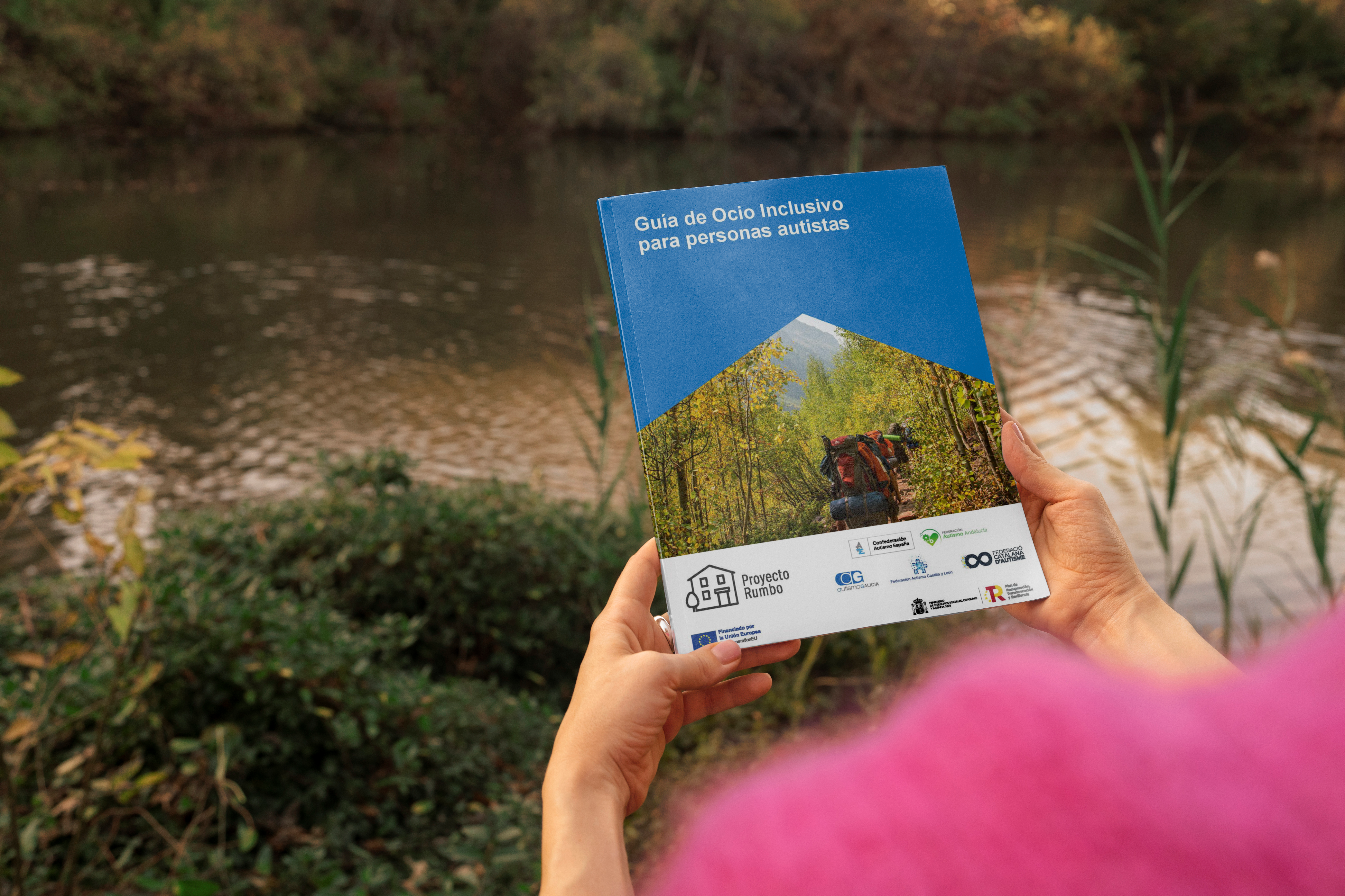 Fotografía en la que una persona en la naturaleza, sostiene la guía de ocio inclusivo para personas autistas.