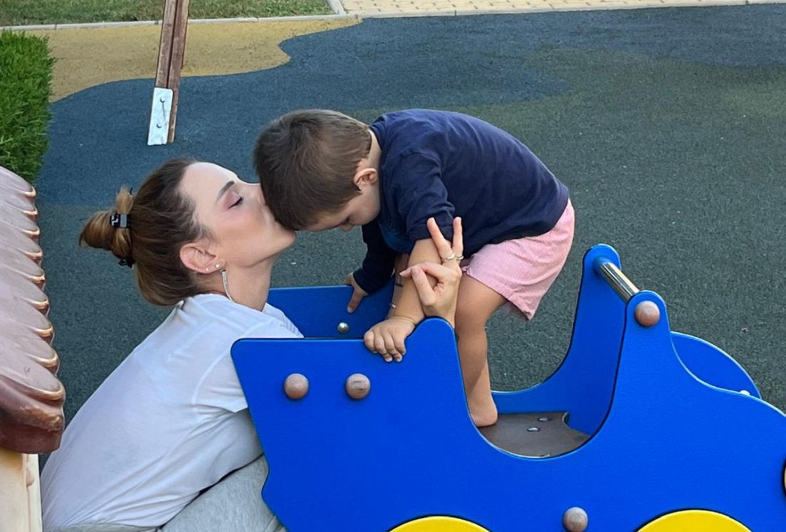 Fotografía de Ana, mamá de Lucas, dándole un beso mientras están en un parque infantil.