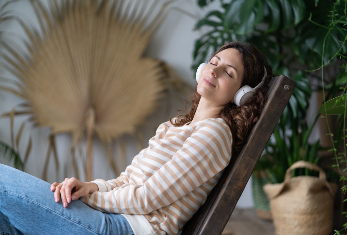 Fotografía de una persona recostada en una silla, con gesto tranquilo y de calma, mientras tiene puestos unas auticulares.