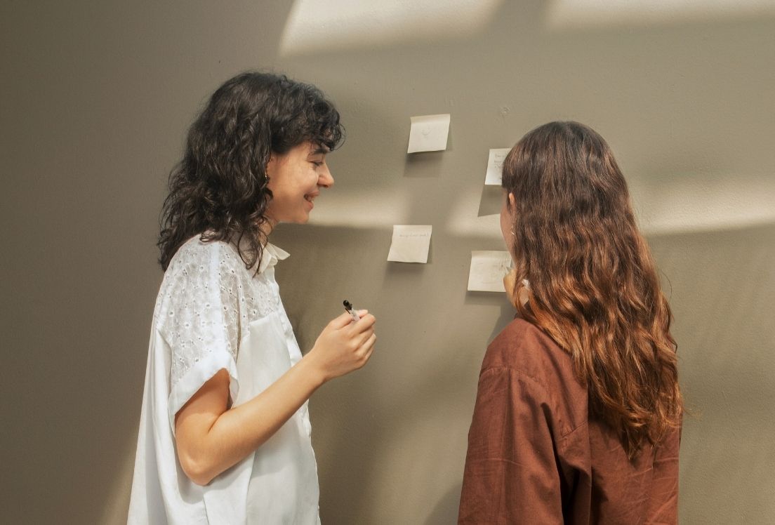 Dos chicas reparten tareas en diferentes papeles que pegan en una pared.