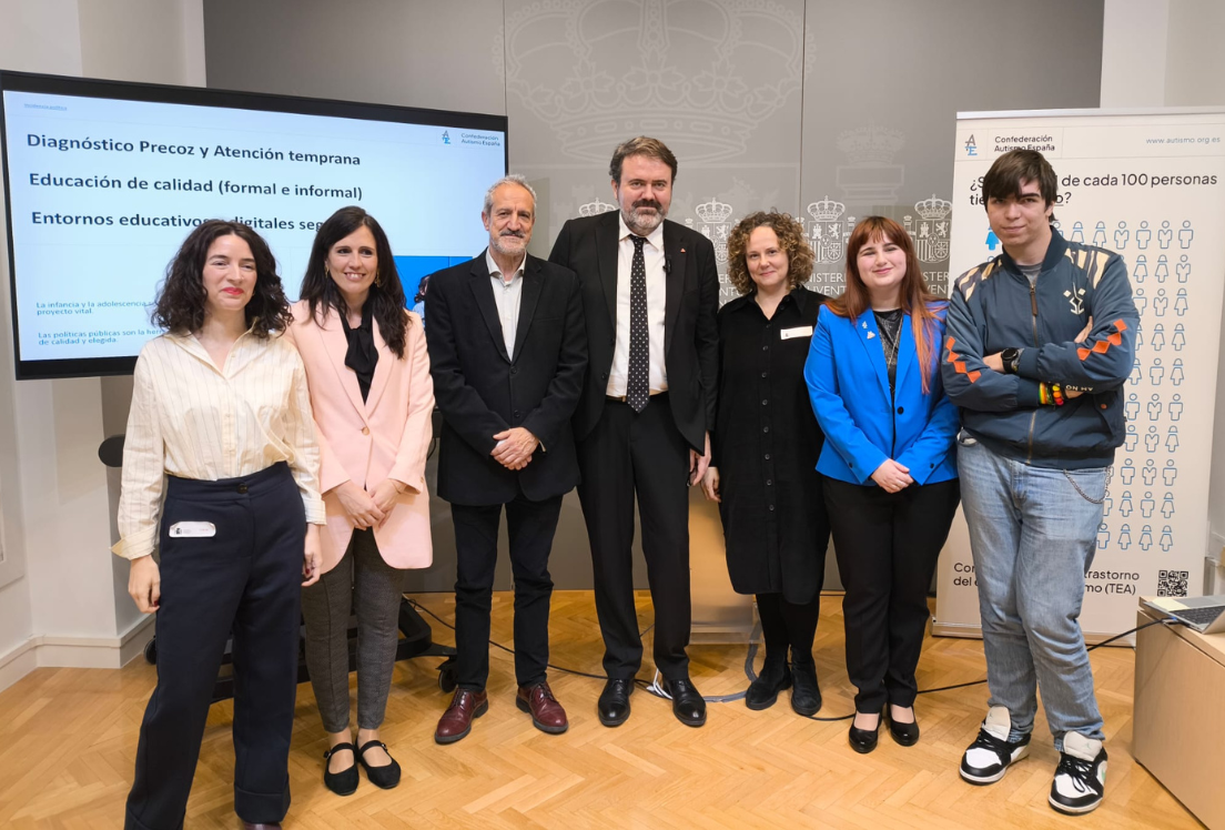 Un grupo de siete personas en una sala, de pie delante de una pantalla.