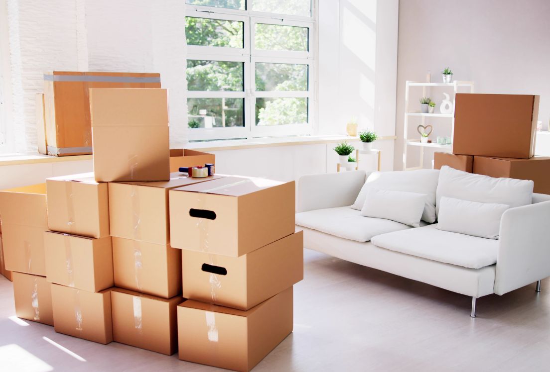 Imagen de un salón con cajas de mudanza y un sofá blanco.