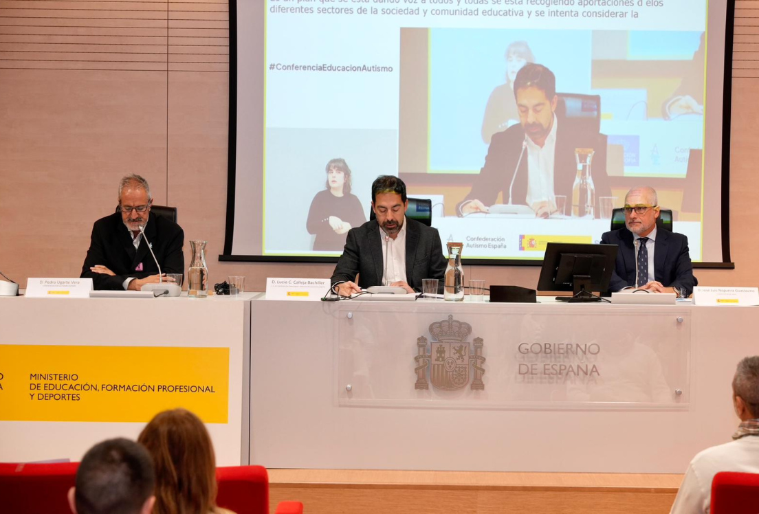 tres hombres sentados a una mesa de presidencia en una conferencia con una pantalla detrás