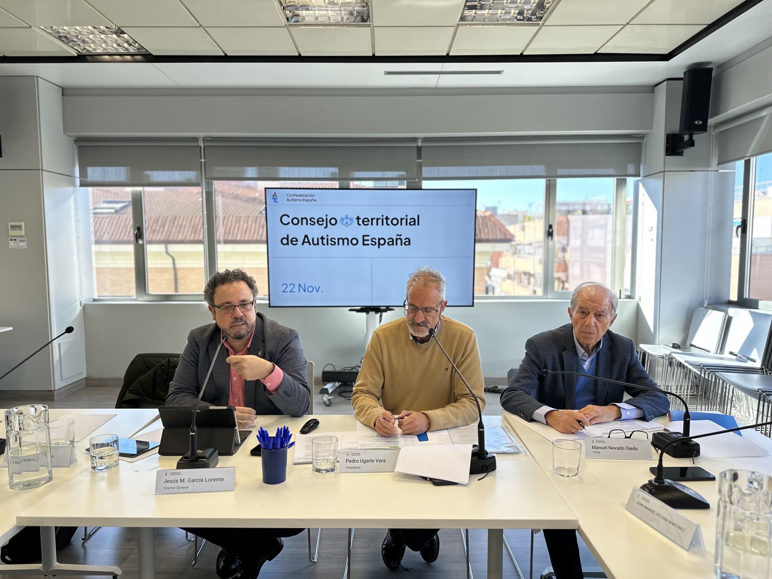 Tres hombres sentados frente a una mesa con una pantalla de TV de fondo