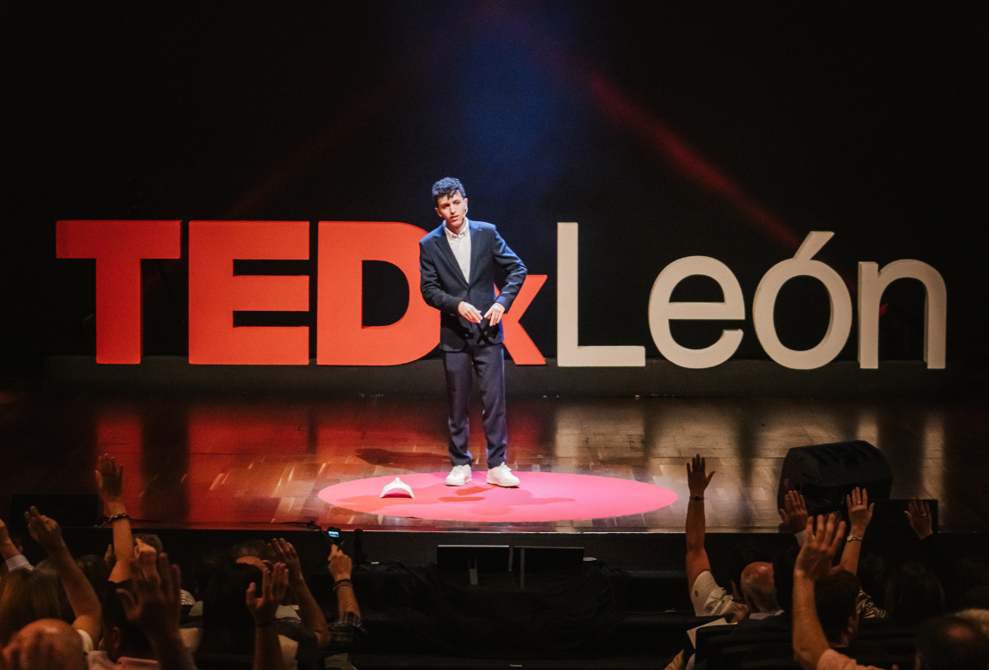 Joven vestido de traje de pie en un escenario, con las letras "TEDx León" detrás