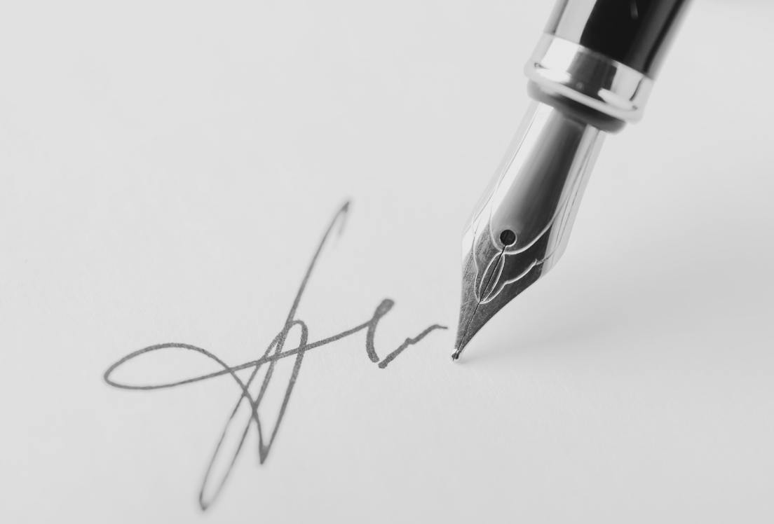 primer plano de una pluma escribiendo una firma en un papel blanco