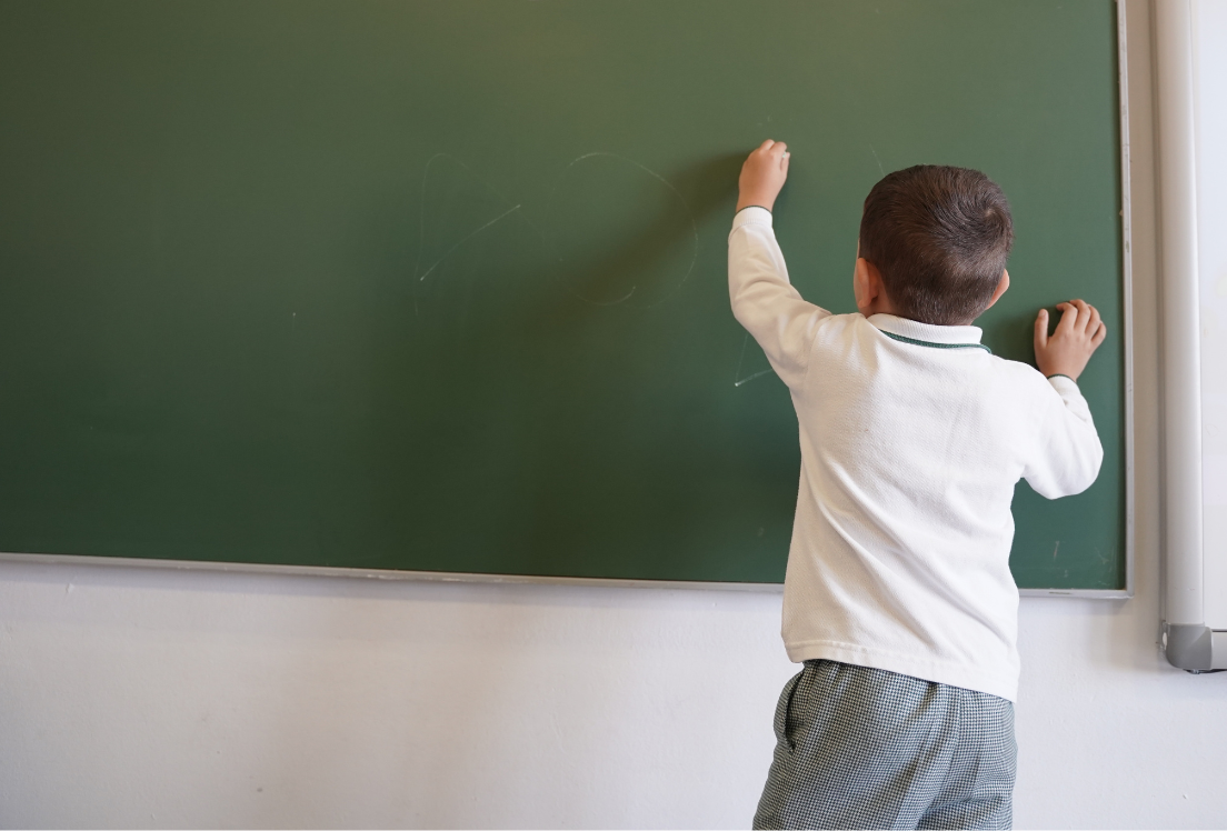 Niño de espaldas escribiendo en una pizarra