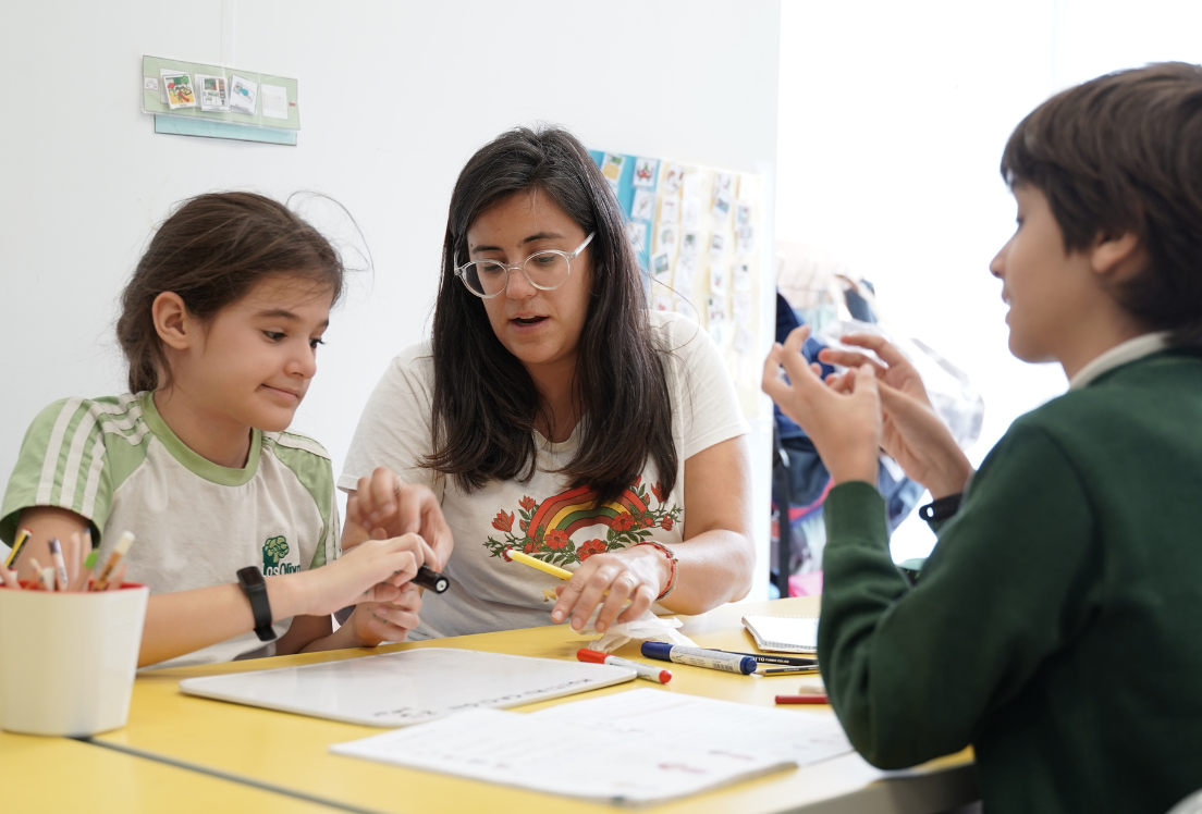 Una niña y un niño trabajan con una profesora en un aula