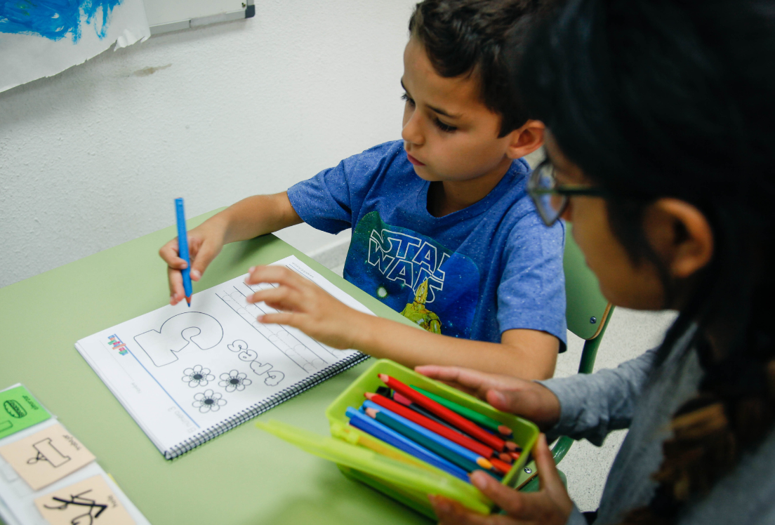 Niño sentado en una mesa haciendo una ficha con su profesora