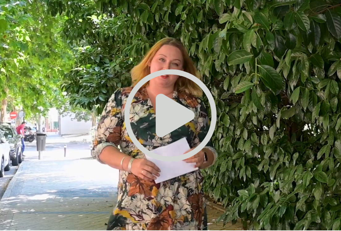 Una mujer andando por la calle con un fondo de hojas verde