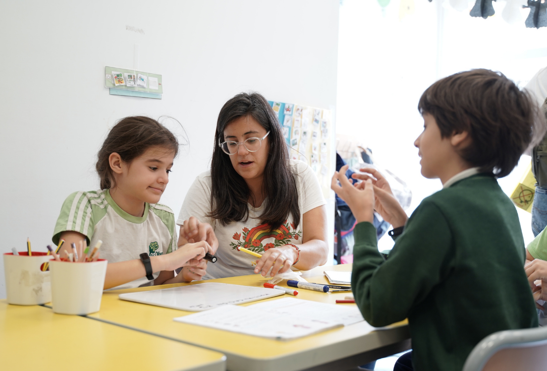 Una profesora junto a una niña con autismo en el fondo, y delante un niño autista de espaldas