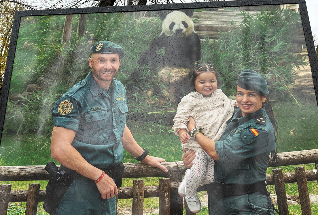una foto de dos guardias civiles con una niña pequeña en brazos y un oso panda al fondo