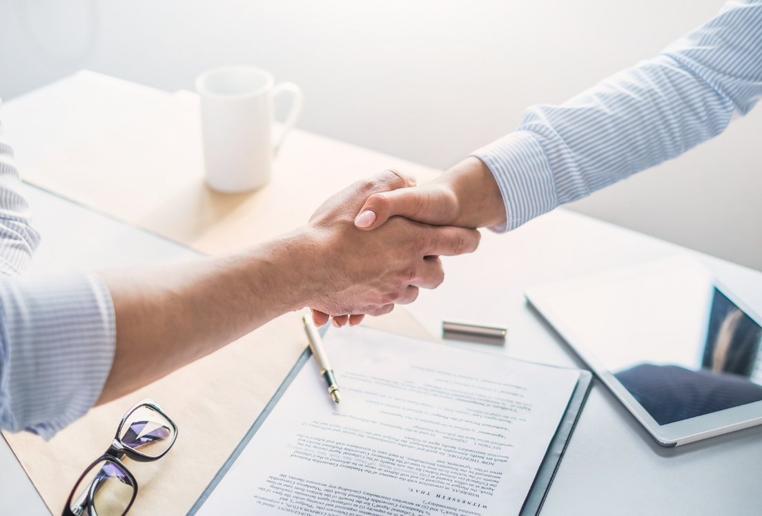 Dos manos estrechándose encima de una mesa de trabajo